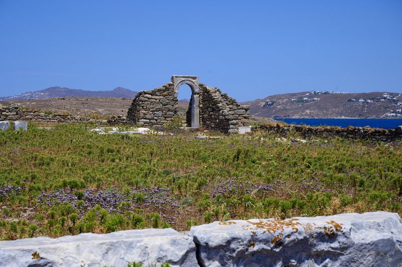 Stenvalv bland ruinerna vid gymnasion på Delos med havet och grannön Mykonos bakom