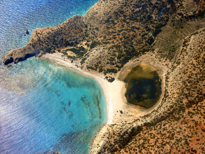 Flygbild över Gavdos kust med turkost vatten, ljus strand och en liten lagun innanför