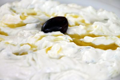En skål tzatziki ringlad med olivolja och garnerad med en oliv, på ett träbord vid havet