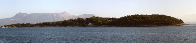 Panorama över den tallbevuxna ön Vido utanför Korfu med Korfus berg i bakgrunden